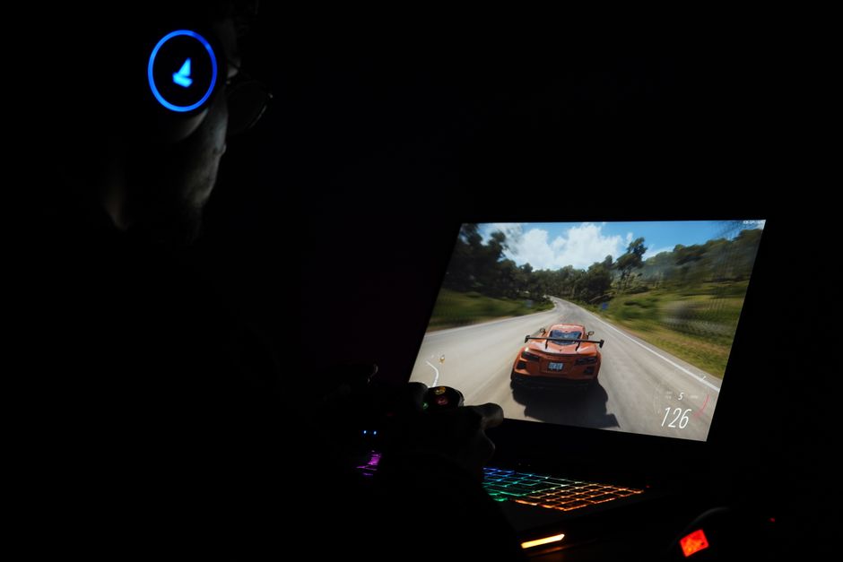 A gamer using a laptop and headphones to play a car racing game in a dark setting.