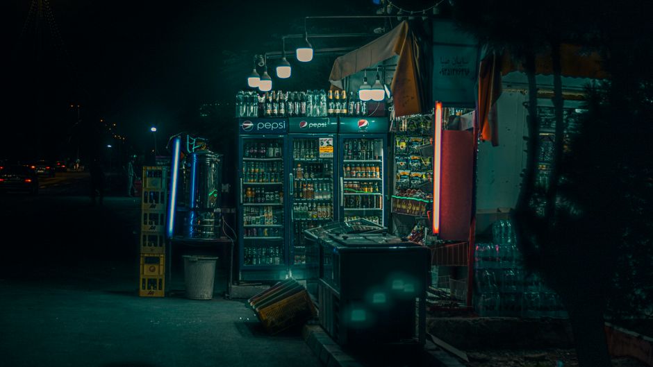 Cozy night view of a street vendor with illuminated beverage fridges and inviting atmosphere.
