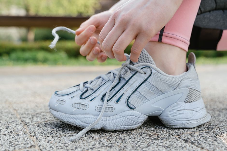 Close-up of a woman tying shoelaces on white sneakers during an outdoor exercise session.