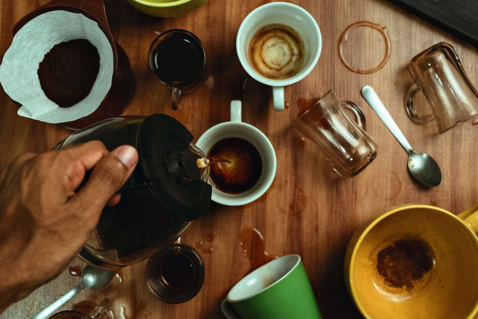 Hand pouring coffee into various cups with spills on wooden table.