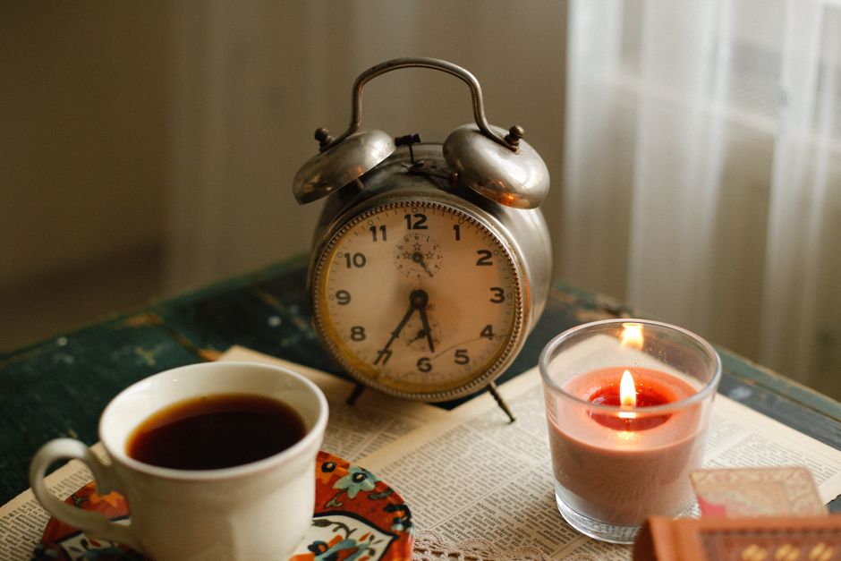 A cozy setting with a vintage alarm clock, coffee, and candle on a table.