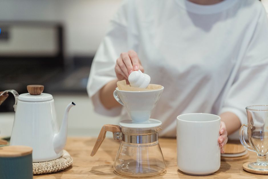 A person prepares coffee using a pour-over method in a modern kitchen setting.