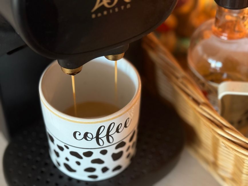 A coffee mug under an espresso machine with golden brew dripping, surrounded by a cozy kitchen setup.