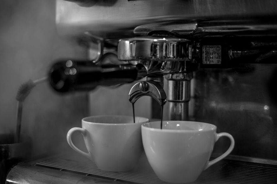 Monochrome image of an espresso machine brewing coffee into white cups.