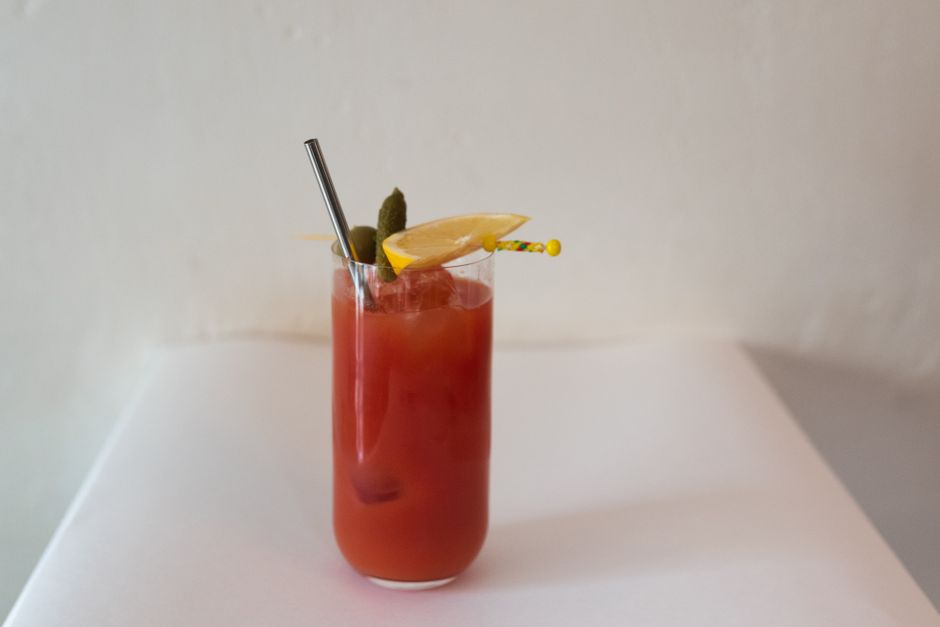 Close-up of a classy Bloody Mary cocktail garnished with pickles and lemon slice on a white background.