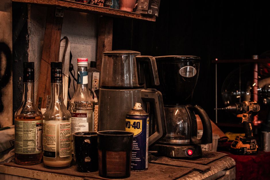 A rustic kitchen counter with a vintage coffee maker, bottles, and tools, evoking a nostalgic ambiance.