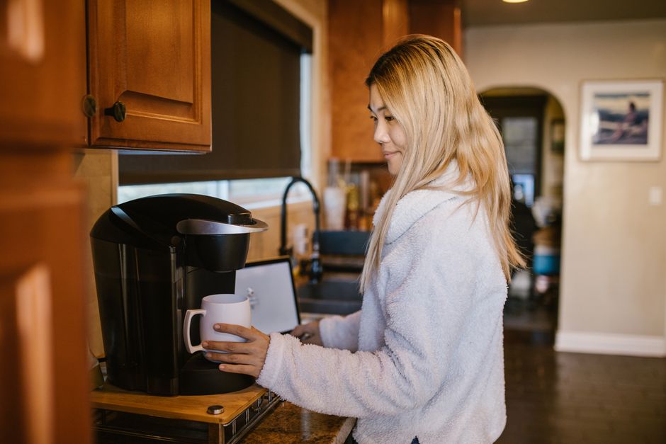 Woman with blonde hair making coffee in a cozy home kitchen setting.