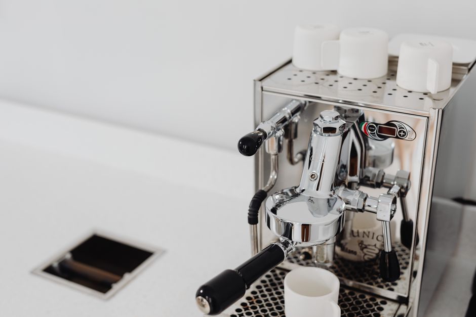 Sleek espresso machine on a white countertop with cups on top, perfect for any modern kitchen.