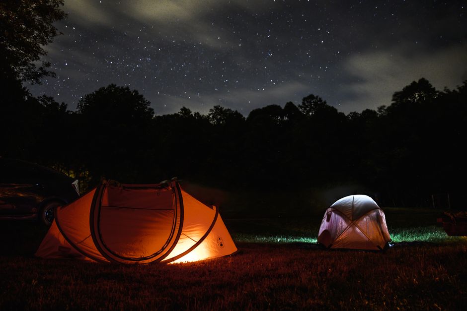 A serene night camping scene with glowing tents under a starlit sky.