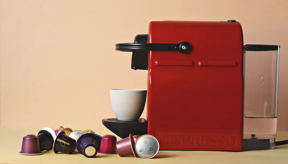 Red coffee machine with assorted capsules and a cup on a beige background.