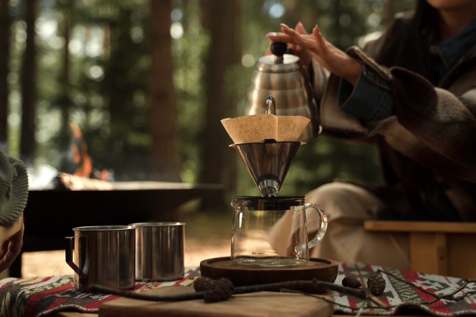A serene outdoor scene capturing a hand brewing coffee with a pour over method, highlighting nature and simplicity.