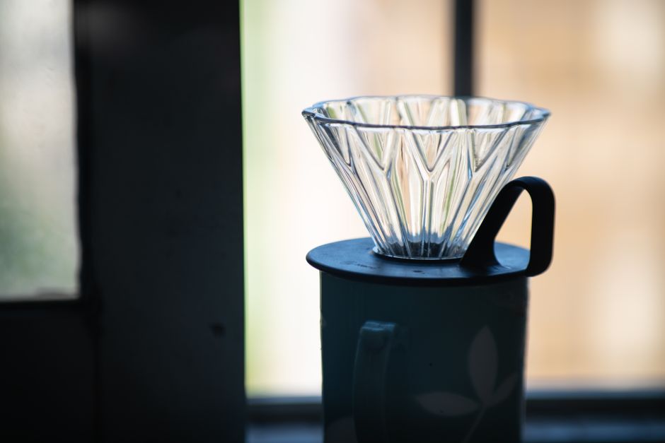 A glass coffee dripper sits atop a mug by a softly lit window, perfect for brewing.