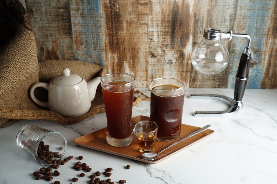 Cold brew coffee and tea on a rustic marble table with a teapot and coffee beans for a cozy morning vibe.
