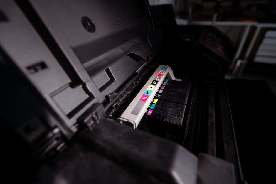 Detailed view of open printer with visible CMYK ink cartridges in a dark setting.