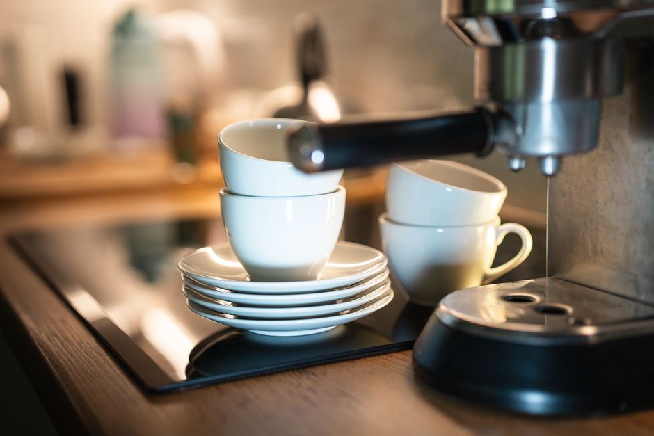 A close-up of an espresso machine with stacked cups in a warm kitchen setting.