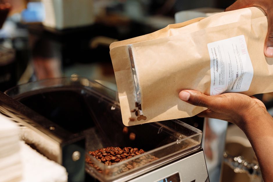 Close-up of hands refilling coffee beans into a coffee grinder at a cafe.