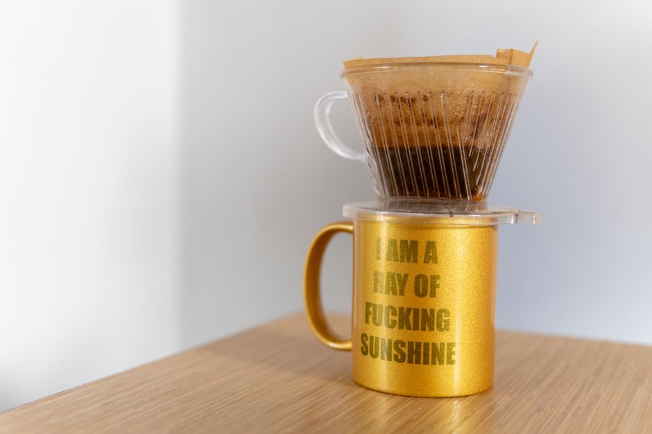 Golden ceramic cup with coffee filter and humorous text setup on a wooden table.
