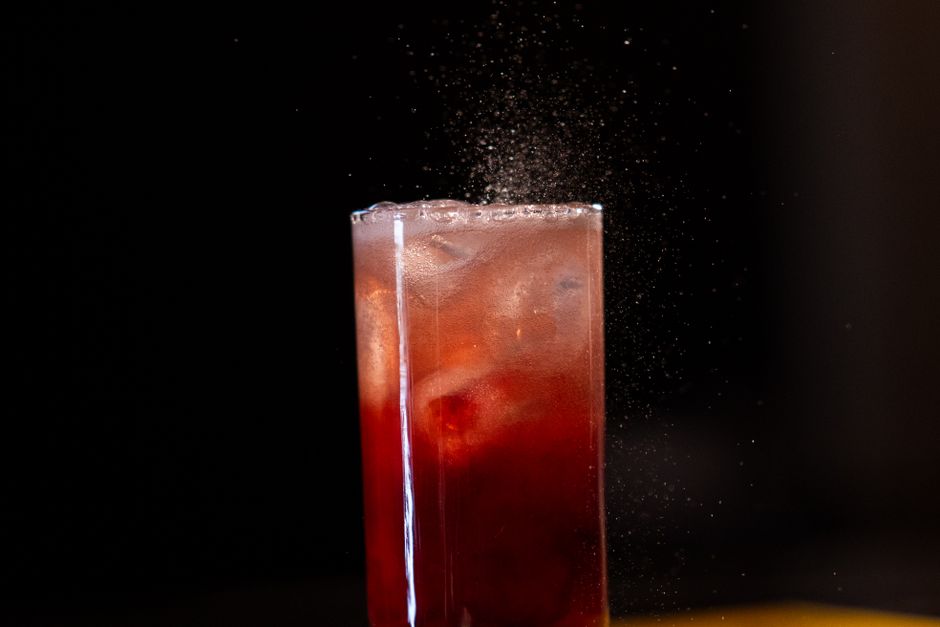 A refreshing red cocktail with ice cubes, exuding elegance against a dark backdrop.