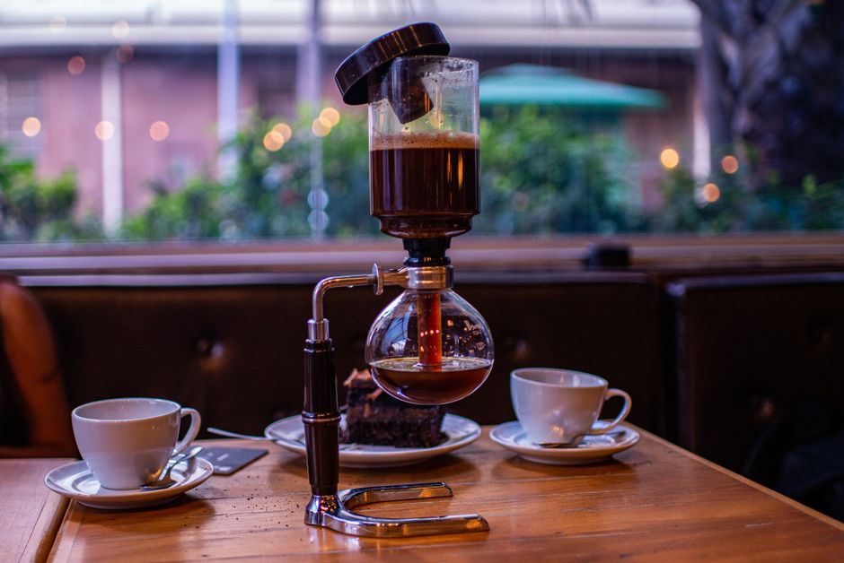 Cozy café corner featuring a syphon coffee maker with cups on the table.