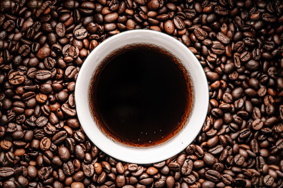Overhead view of a cup of black coffee surrounded by roasted coffee beans for a rich aroma.