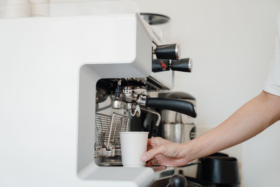 Person's hand using an espresso machine to prepare coffee. Modern kitchen setting.