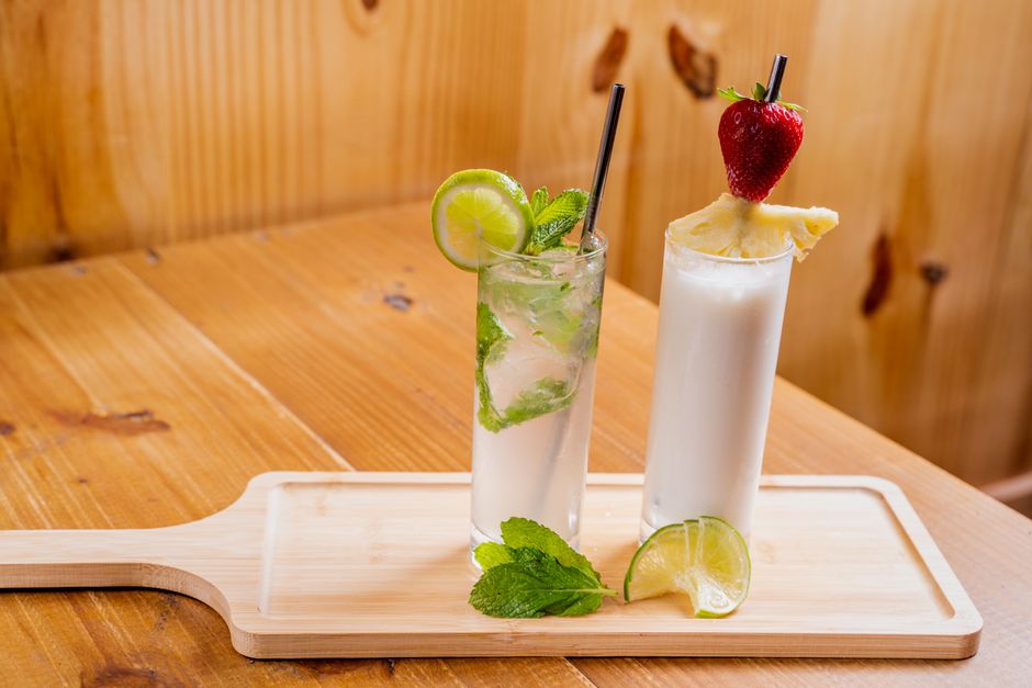Two tropical cocktails with lime, mint, and fruit garnish on a wooden tray, perfect for summer.
