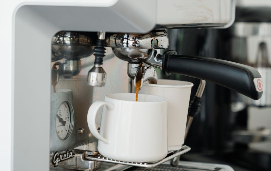 Coffee machine pouring fresh brewed aromatic coffee into ceramic mug and disposable cup