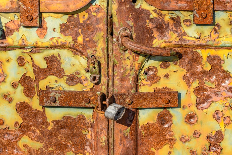 Close-up of an aged, rusted padlock on a corroded metal door with peeling paint.