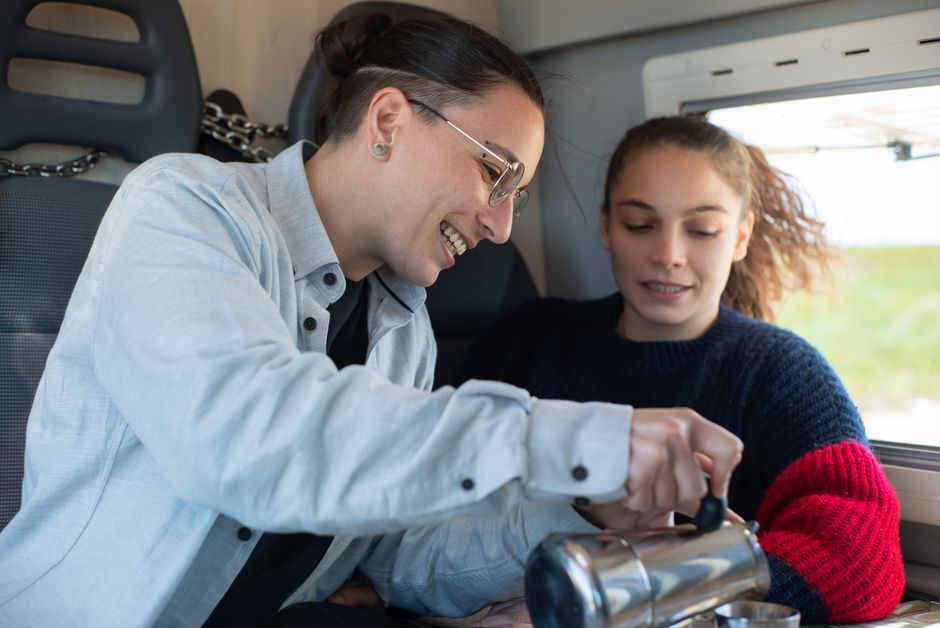 A joyful couple pours coffee in a motorhome, capturing a cozy travel moment.