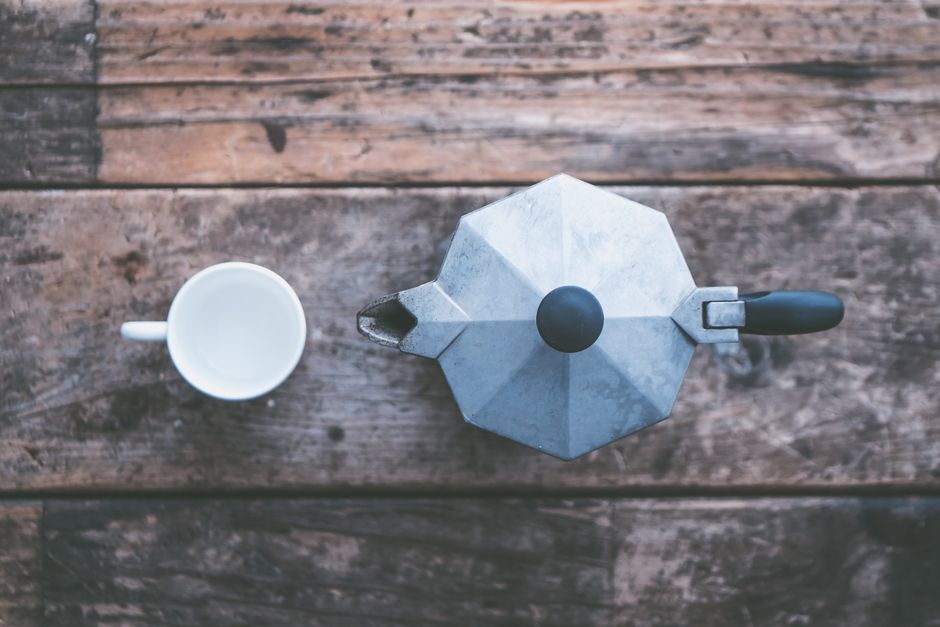Top view of a metal moka pot and cup on a rustic wooden table, evoking a classic style.