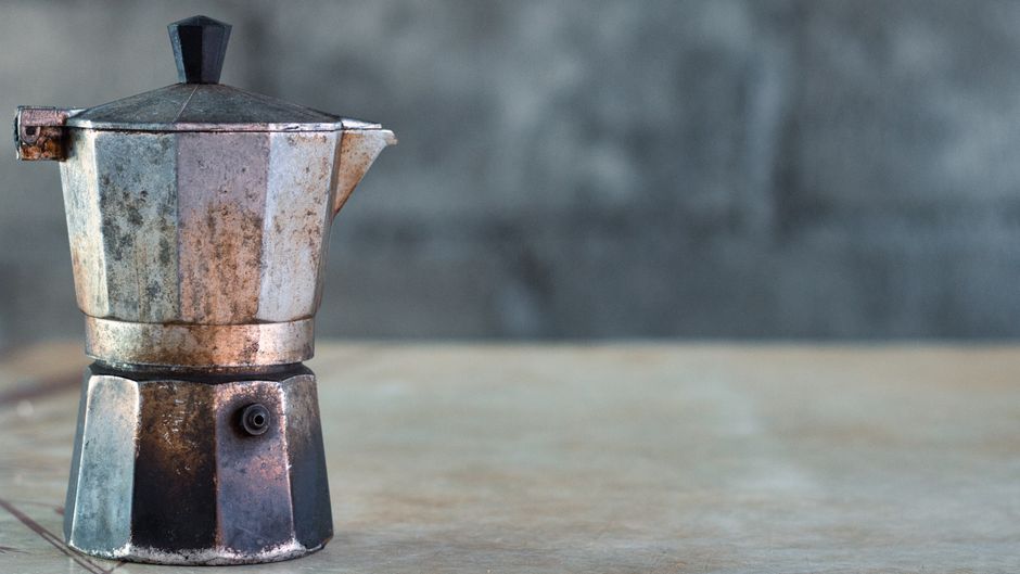 Aged metal Moka pot with worn texture on rustic background, classic still life setup.