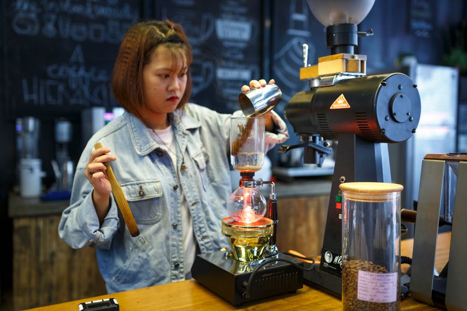 Barista using a coffee siphon in a cozy cafe setting, preparing a fresh brew.