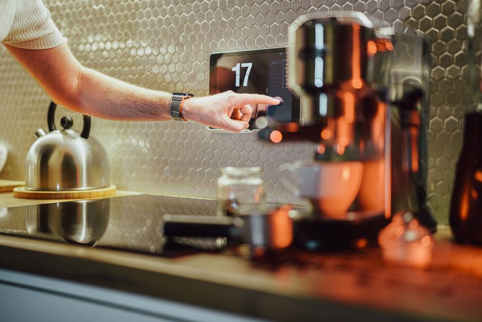 A man interacts with a touchscreen in a stylish kitchen setting, featuring modern appliances.