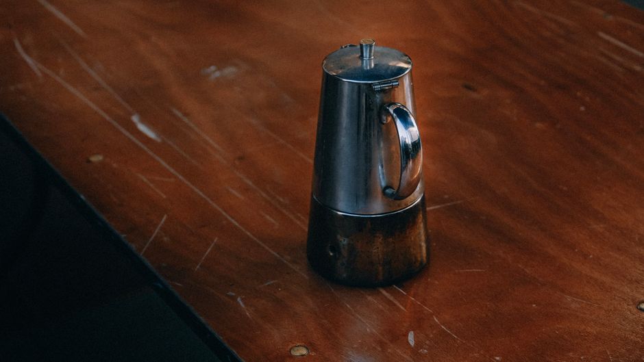 A classic stainless steel coffee pot resting on a rustic wooden table.