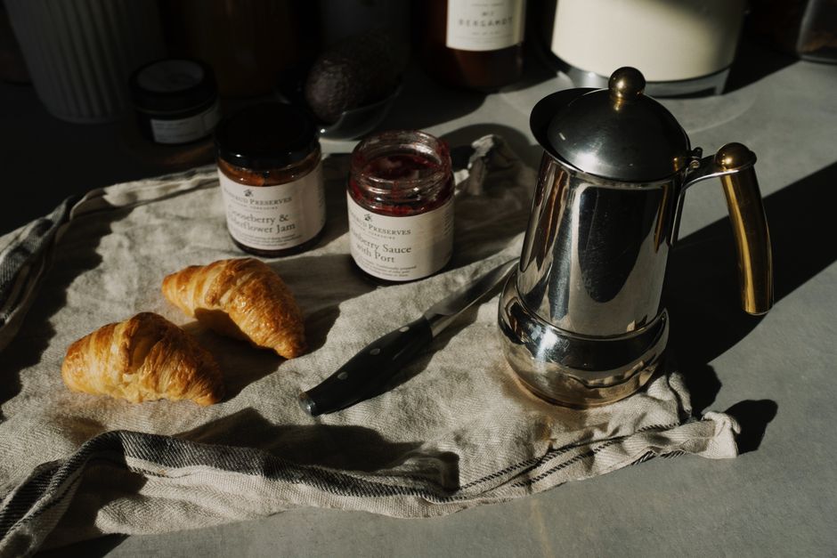 A cozy morning breakfast featuring croissants, jam, and coffee on a rustic cloth.